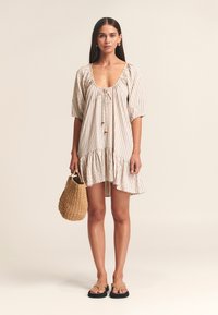 Gestreepte jurk met korte mouwen, geplooide halslijn en ruches aan de zoom, gemaakt van lichtgewicht stof. Gecombineerd met een geweven tas en platte sandalen.