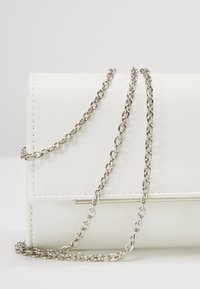 Borsa a mano in pelle bianca con tracolla a catena argentata, caratterizzata da un design rettangolare elegante e dettagli di cuciture sottili.