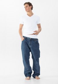 Witte V-hals t-shirt met een slimfit ontwerp, gecombineerd met oversized blauwe spijkerbroeken, met een knoopsluiting en een comfortabele pasvorm. Blote voeten.