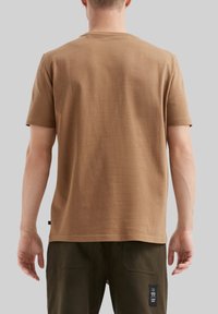 T-shirt marrone a girocollo realizzato in tessuto morbido, caratterizzato da maniche corte e una vestibilità dritta, con cuciture in vista e una piccola etichetta sull'orlo.