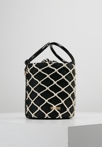 Czarna skórzana torebka z białym plecionym wzorem, wyposażona w okrągłe czarne uchwyty i złoty akcent z logo z przodu.