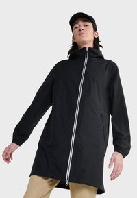 Giacca nera impermeabile con zip frontale completa, dettagli in zip bianca e polsini elasticizzati. Vestibilità lunga e ampia con cappuccio.