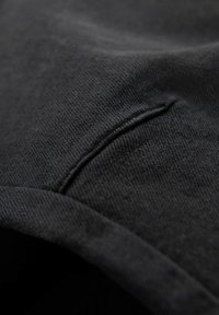 Tejido negro con una superficie suave y texturizada. Presenta una costura y una ligera curvatura, lo que indica un diseño de prenda. Sin patrones ni adornos.
