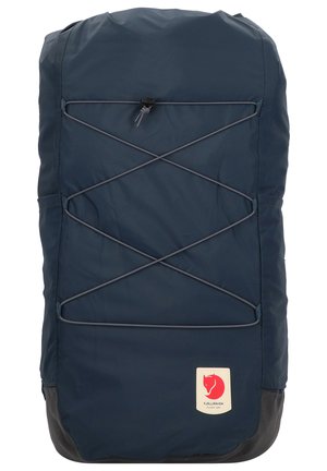 Navy blue backpack with a smooth texture, featuring a bungee cord design, gray accents, and a red logo patch at the bottom.