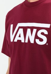 Burgundská bavlněná trička s výrazným bílým logem Vans přes hruď. Klasický design s kulatým výstřihem a krátkými rukávy.