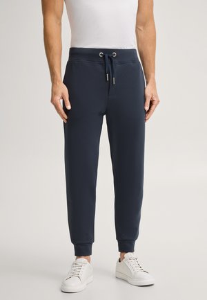 Uomo che indossa pantaloni jogger blu navy con vita con coulisse e caviglie risvoltate, abbinati a sneaker bianche e una t-shirt bianca.
