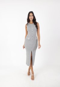 Graues geripptes Midi-Kleid mit Knöpfen vorne, zwei aufgesetzten Taschen und einem Schlitz vorne. Das Model trägt transparente Absatzsandalen.