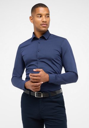 Dunkelblaues langärmliges Hemd mit Button-Down-Kragen, glatter Textur und subtiler Glanz. Kombiniert mit dunklen Hosen und einem schwarzen Gürtel.