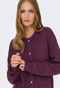 Bordeauxroter Strickcardigan mit Rundhalsausschnitt, verziert mit Perlenknöpfen, strukturiertem Stoff und langen Ärmeln, bietet eine lockere Passform.