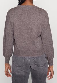 Brauner, gestrickter Pullover mit lockerer Passform, Ballonärmeln und gerippten Bündchen, kombiniert mit grauen, hochtaillierten Jeans.