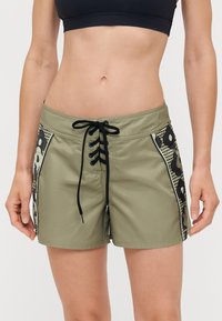 Shorts de bain vert olive avec fermeture à lacets à l'avant. Présentent des accents latéraux noirs et à motifs ainsi qu'une texture de tissu lisse.