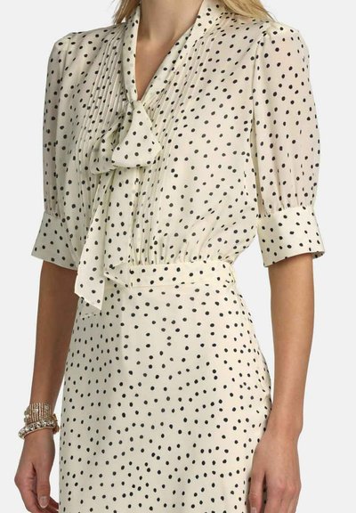 Krém színű blúz fekete pöttyökkel, rövid légies ujjakkal és pliszírozott elejjel. Megkötős nyakrész és passzés derékrész. Sima, könnyű anyag.