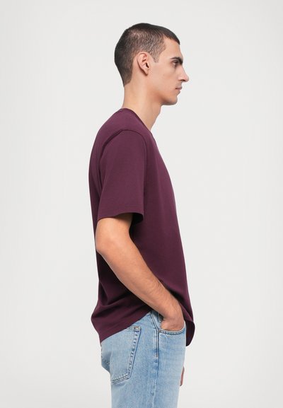 Camiseta corta de manga corta color burdeos con cuello redondo, diseño sencillo y corte relajado, combinada con jeans de denim azul claro. Con detalles mínimos.