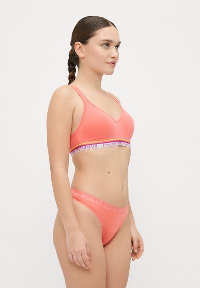 Coral lingerie set featuring a wireless bralette and matching thong. Soft fabric, v-neck design, and branded elastic bands with subtle logo detail.