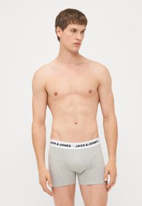 Graue Baumwoll-Boxershorts mit einem weißen Bund, der das "JACK & JONES"-Logo zeigt. Die Passform ist eng und der Stoff wirkt weich und glatt.