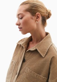 Camicia in corduroy beige, con chiusura a bottoni, due tasche applicate e colletto. Tessuto liscio con righe verticali.
