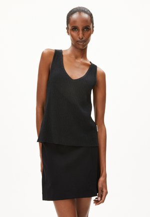 Top in cotone nero a costine con scollo a V e spalline larghe, abbinato a una mini gonna nera aderente. Entrambi i capi sono realizzati in tessuto morbido.