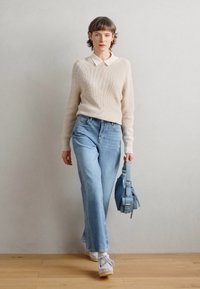 Beige strikkegenser med hvit krage, lyseblå vid jeans, hvite joggesko og en lyseblå veske. Teksturen er myk og stilen er avslappet.