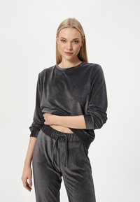 Harmaa velour-loungewear-asuste, joka sisältää pitkähihaisen paidan, jossa on pyöreä kaula-aukko ja rento istuvuus, yhdistettynä joustavaan vyötäröön. Pehmeä, teksturoitu kangas.