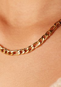 Gouden metalen ketting met elkaar verbonden schakels. Glad, glanzend oppervlak met een stevige en gedurfde uitstraling. Close-up weergave tegen de huid.