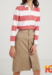 Gestreepte lange mouw polo in koraal en wit, gecombineerd met een beige rok met knopen aan de voorkant. De rok heeft een zijsplit en een gladde textuur.