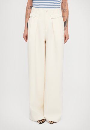 Prispôsobené krémové široké nohavice s záhybmi, bočnými vreckami a vysokým pásom. Textúrovaná tkanina a kontrastné topánky s potlačou zvieracej kože.