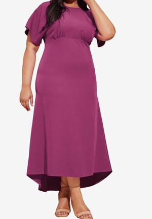 Femme portant une robe midi violette à manches papillon et ourlet asymétrique, associée à des sandales fines couleur nude.
