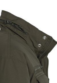 Oliwkowo-zielona kurtka z wysokim kołnierzem, wyposażona w kieszeń na zamek błyskawiczny, zatrzaski oraz gładką teksturę tkaniny. Widoczne detale przeszyć.