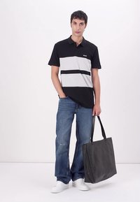 Svart og gråstripete polo-shirt med krage, kombinert med lyseblå jeans og hvite joggesko. Bærer en mørkegrå håndveske.