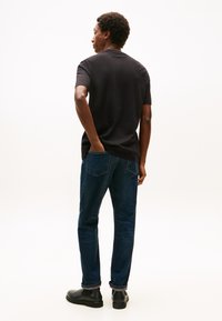 Črna majica, modre kavbojke in črni čevlji. Denim ima strukturiran videz, tkanina majice pa je videti gladka. Model stoji bočno.