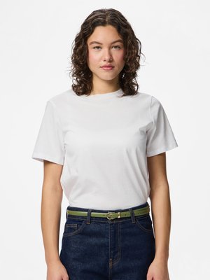 T-shirt bianca in cotone con maniche corte, abbinata a jeans di denim blu e una cintura verde con fibbia dorata. Design e vestibilità semplici.