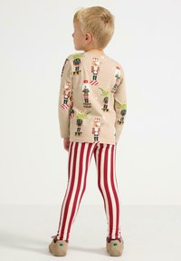 Beige langærmet top med nutcracker-tryk, parret med rød-hvide stribede leggings. Stoffet ser blødt ud; detaljer inkluderer mønstre på begge dele.