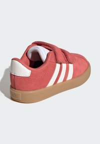 Ružové semišové tenisky s bielymi pruhmi, zapínaním na suchý zips a béžovou gumovou podrážkou. Okrúhla špička a polstrovaný golier pre pohodlie.