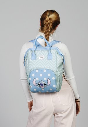 Mochila de color azul claro con patrón en zigzag, presenta un bolsillo azul con lunares blancos y un diseño del personaje Stitch. Dos asas de transporte.