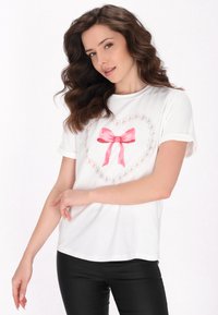 Hvid bomulds-T-shirt med en hjerteform lavet af små pink hjerter og en lyserød satinbue i midten. Korte ærmer og løs pasform.