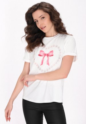 Hvid bomulds-T-shirt med en hjerteform lavet af små pink hjerter og en lyserød satinbue i midten. Korte ærmer og løs pasform.