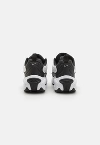 Zwart-witte sportschoenen met een ronde vorm, gladde en gestructureerde materialen, en zichtbare "AIR" branding op de hak.