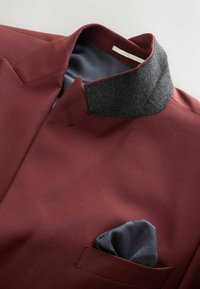 Bordó zakó texturált szürke gallérral és kék díszzsebkendővel a mellzsebben, sima anyagból és szabott kialakítással.