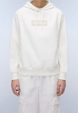 Person iført en off-white hættetrøje med en rektangulær logo på brystet og matchende off-white cargobukser.