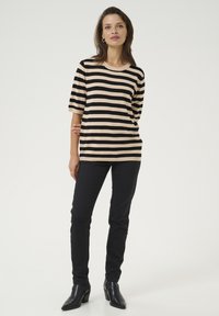 Haut rayé beige et noir, en tissu tricoté, coupe décontractée avec des manches courtes. Associé à un pantalon noir ajusté et des bottines noires.