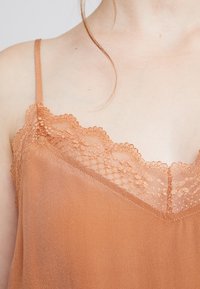 Kobberfarvet cami-top med fint blondertrim langs udskæringen, glat stof, justerbare stropper og en afslappet pasform.