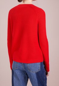 Punainen neulottu villapaita, jossa on ribbineulos ja raglansuut. Yhdistetty vaaleansinisten farkkujen kanssa, jotka ovat rentoa istuvuutta ja rentoa tyyliä.