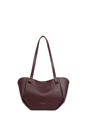 Sac à main en cuir marron foncé avec de longues anses et le logo Lancaster Paris doré sur le devant, présenté sur fond blanc.