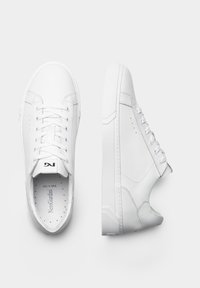 Zapatillas blancas con material de cuero suave, puntera redonda, diseño de cordones, lengua plana y suela de goma texturizada con una sutil marca.