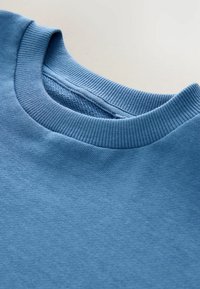 Hellblaues Sweatshirt mit geripptem Rundhalsausschnitt, aus weichem Stoff. Die Textur ist glatt, und der Kragen hat eine kontrastierende Innenlage.