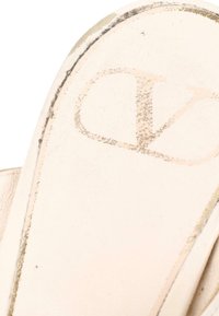 Gros plan de la semelle usée d'une chaussure beige avec un logo "V" imprimé estompé.