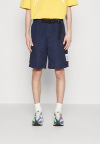 Námornické cargo šortky s elastickým páskem a černým opaskem, obsahující dvě boční kapsy a nášivku. Vybavené multibarevnými teniskami a bílými ponožkami.