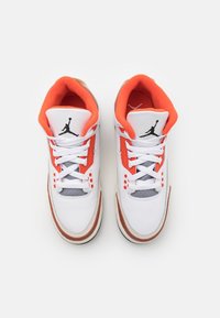 Sneakers in pelle bianca con accenti arancioni e grigi, dotati di lacci, colletto imbottito, forature e un logo Jumpman nero sulla linguetta.
