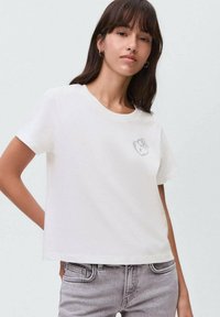 T-shirt en coton blanc avec un col rond et des manches courtes, présentant un petit graphique de bear simple sur la zone gauche de la poitrine.