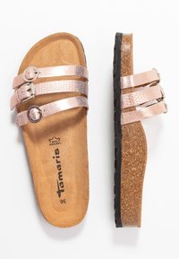 Růžově zlaté skluzné sandály s dvěma texturovanými popruhy, nastavitelnými přezkami a korkovou stélkou. Černá gumová podešev s vlnkovým vzorem.